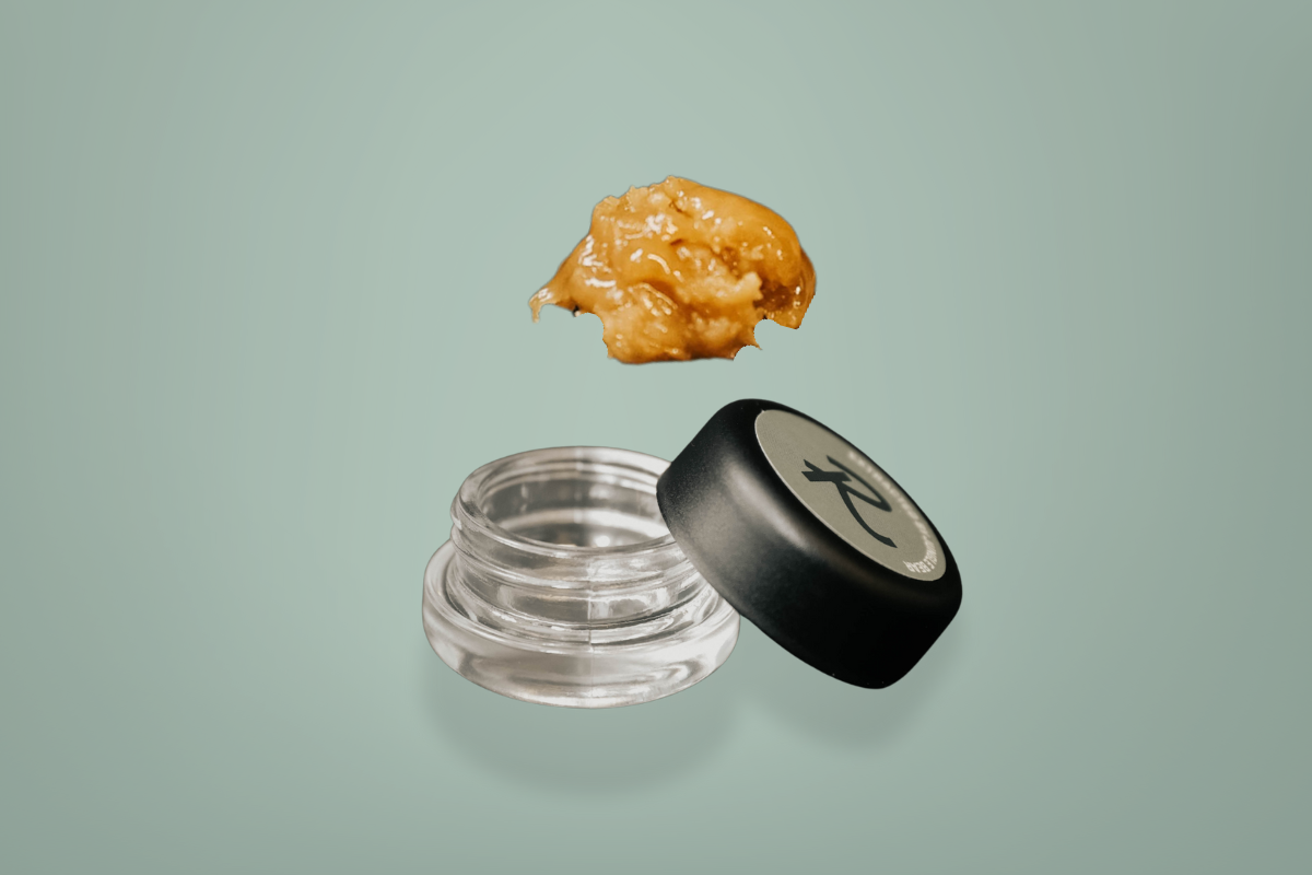 Live hash rosin made by Revival: Farm.Lab.Market, featuring a golden, cold-cured concentrate hovering above an open glass jar with the signature “R” lid, showcasing the creamy texture and solventless quality of Power Plant Live Hash Rosin.