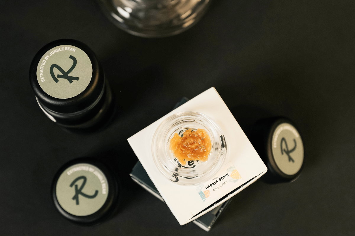 Papaya Bomb Live Rosin, an indica-leaning hybrid, shown in an open jar with creamy golden texture, highlighting its tropical and floral aroma, smooth consistency, and solventless, cold-cured production